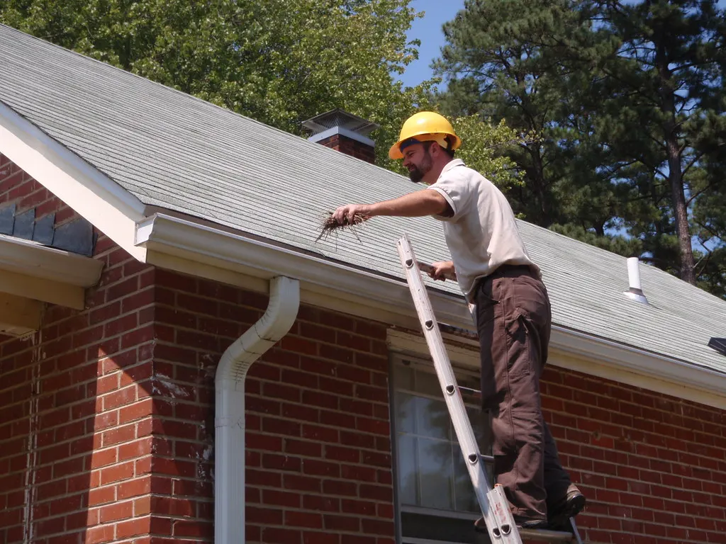 Man on a ladder cleaning out a house gutter