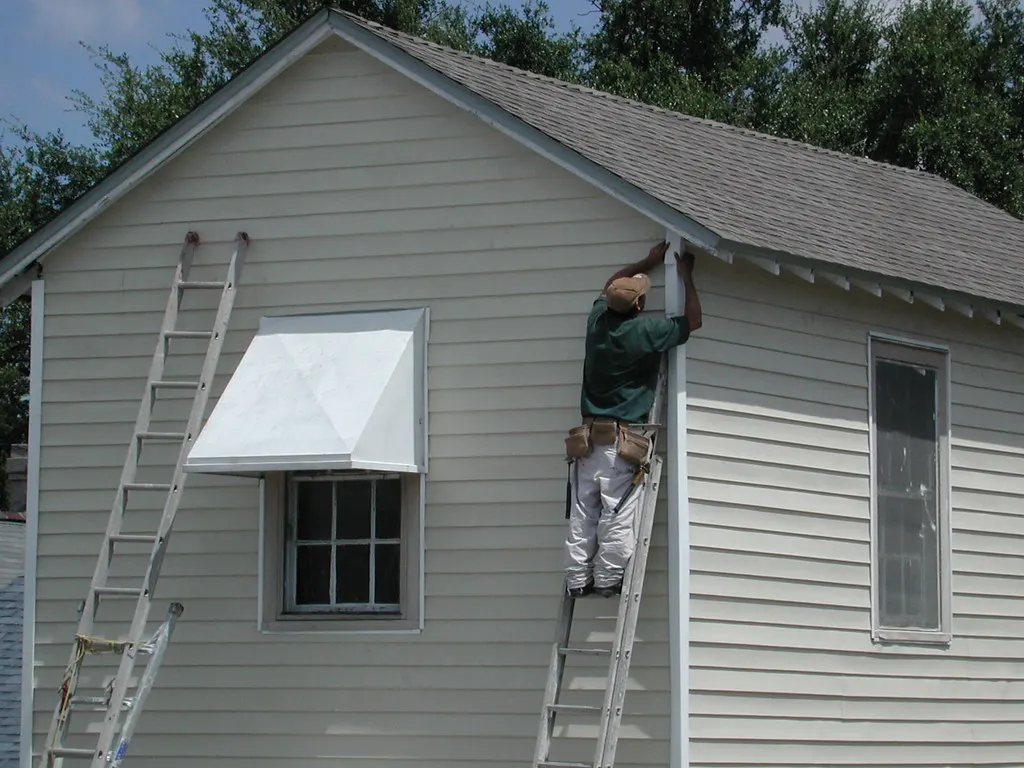 Worker on a ladder installing siding on a house